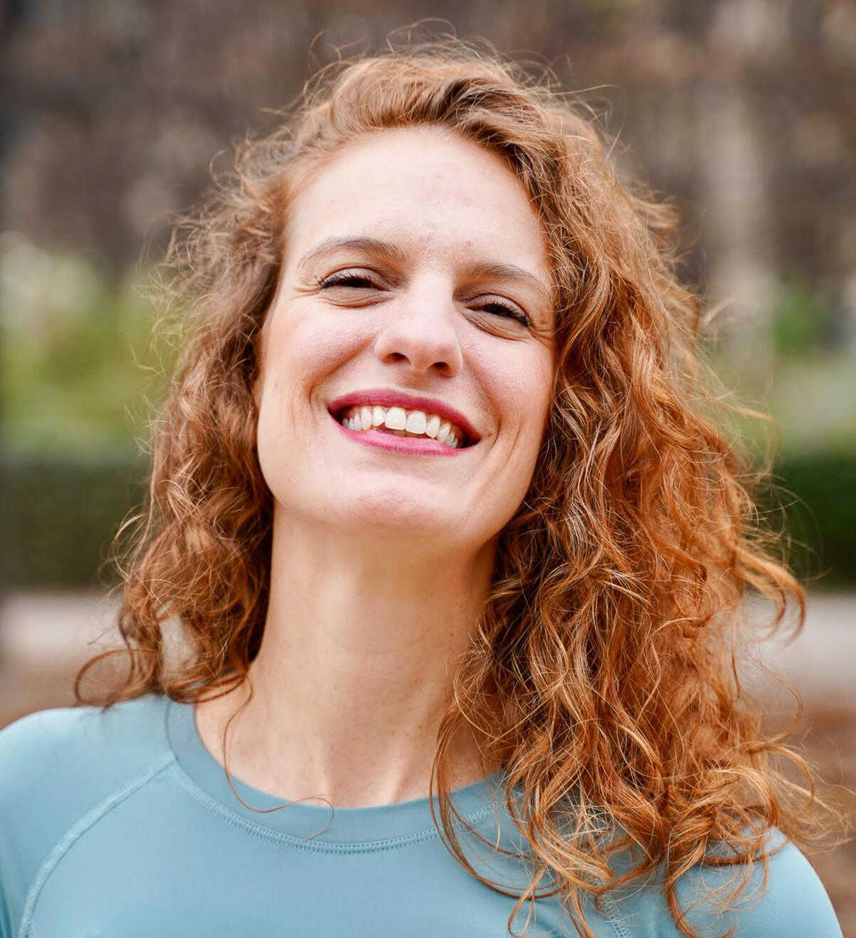 Camila bio picture Camila smiling in a red top and leafy background